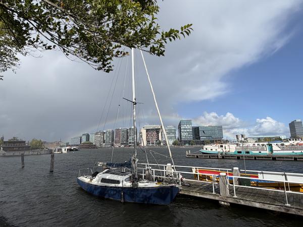 A picturesque view of Oosterdok, Rapenburg, Amsterdam, features a sailboat moored at a dock with modern buildings lining the distant shore